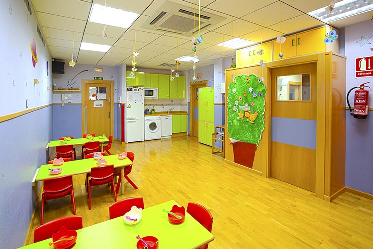Aula Comedor de la escuela infantil Educamar con mesas de color verde y cocina al fondo.