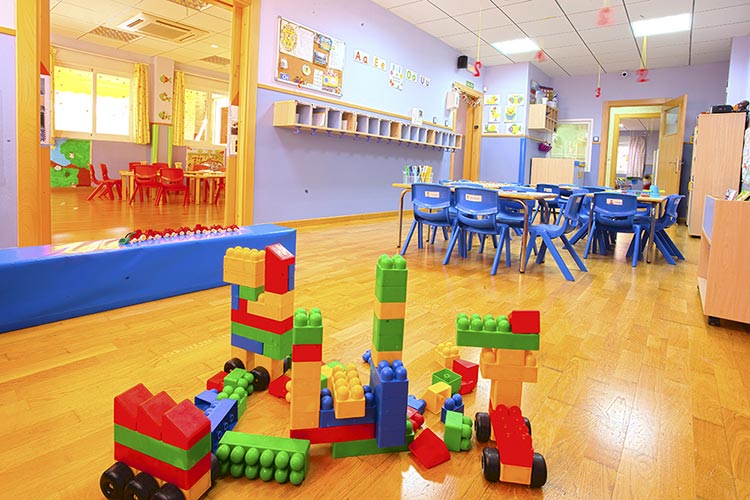 Aula de la escuela infantil Educamar con bloques de juguetes en el suelo y mesas y sillas al fondo.