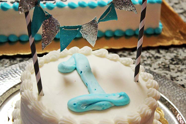 Tarta de cumpleaños decorada con un 1 de color azul y banderines azules y grises.
